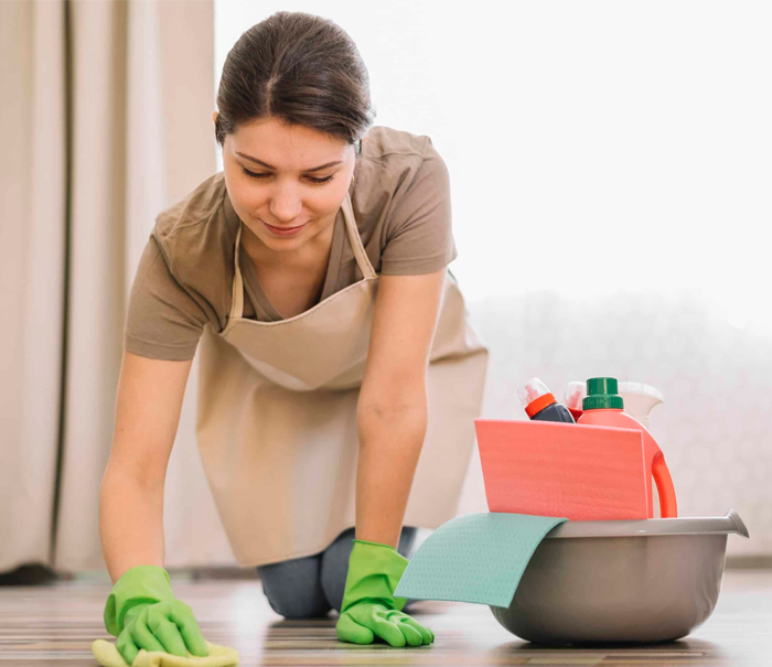 Cleaner wiping a timber floor beside a caddy of cleaning products